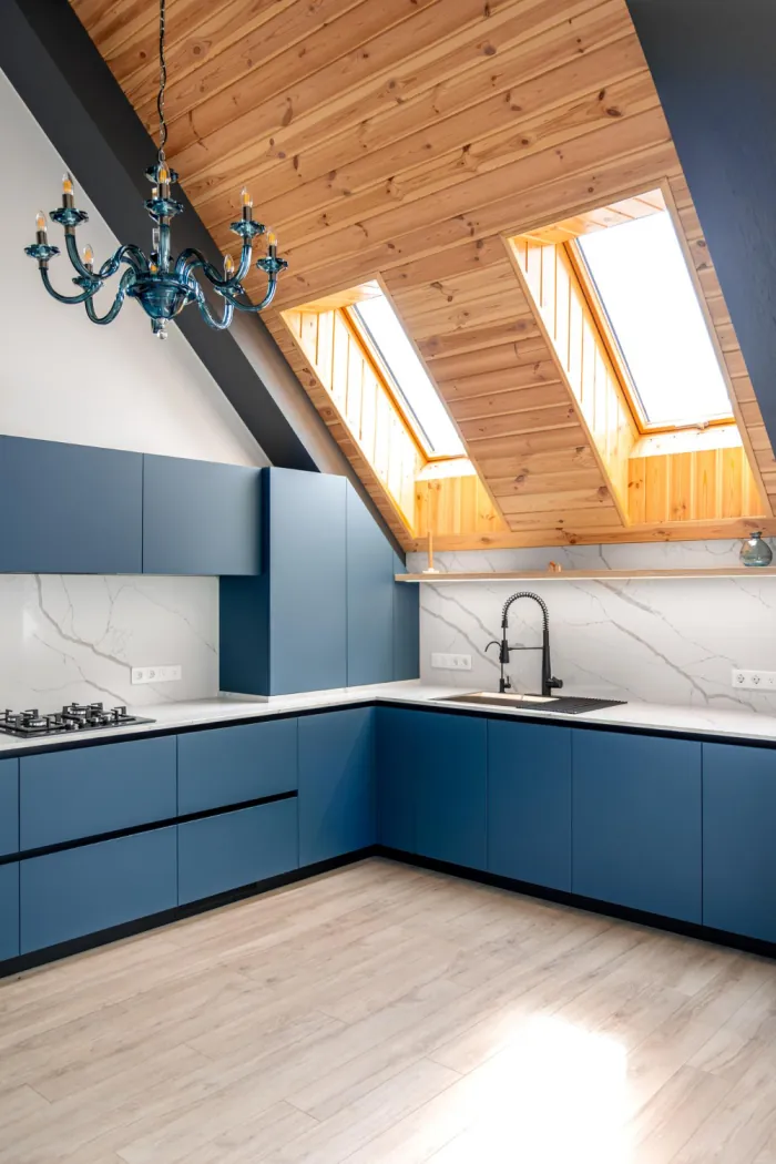 Renovated kitchen with matte blue cabinets, a marble backsplash and skylights set into a timber lined ceiling