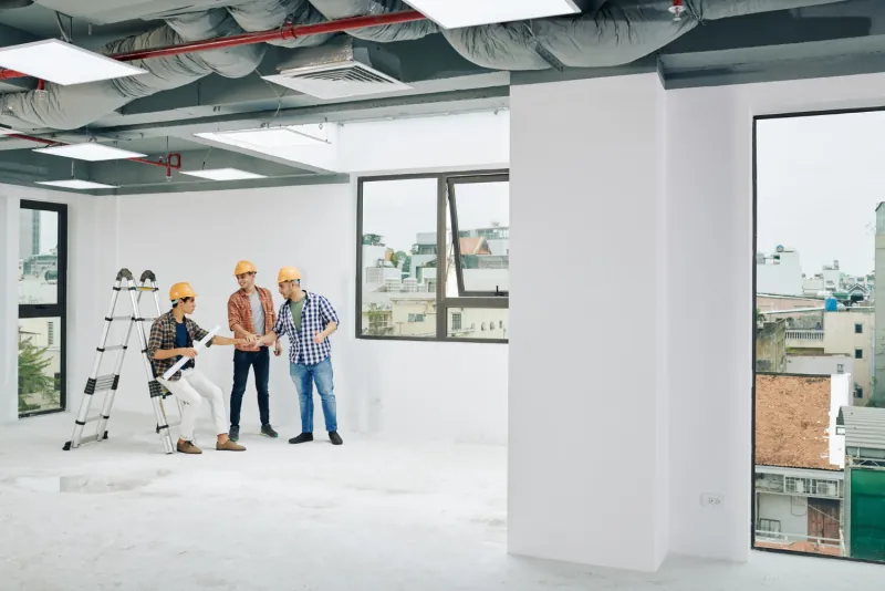 Three contractors in hard hats walking a stripped commercial floor and reviewing the work ahead