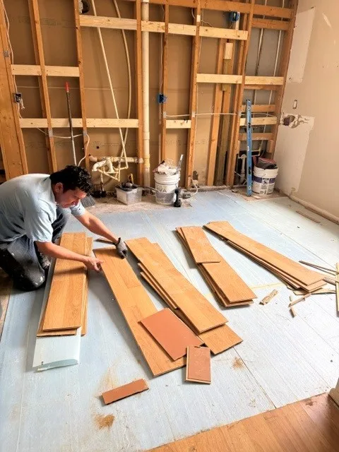 Installer kneeling to lay hardwood flooring planks during a home renovation