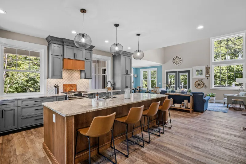 Remodeled open plan kitchen with a large stone island, wood flooring and shaker cabinets