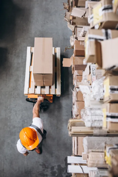 Warehouse worker in a high visibility vest moving palletized boxes during a working shift