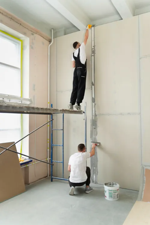 Two workers on a scaffold plastering and finishing a new office partition wall