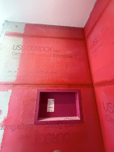 USG Durock cement board part coated in red waterproofing membrane, with the niche formed and the mixing valve inlet sealed