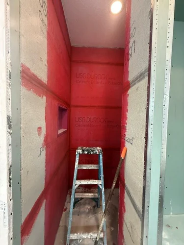 Shower enclosure lined in USG Durock cement board and coated in red waterproofing membrane, with the niche formed into the wall