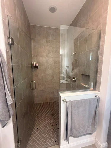 The original shower before work, lined in square taupe tile with a small mosaic floor and a half height glass panel