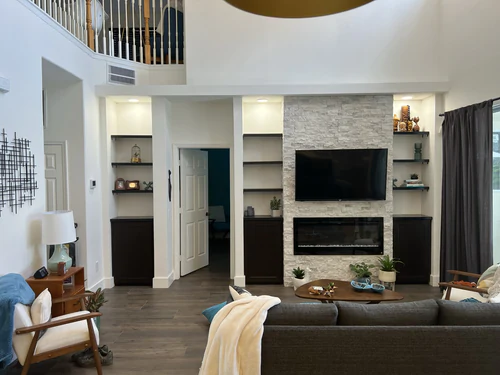 Finished two story living room with a stacked stone fireplace wall, built in shelving and plank flooring
