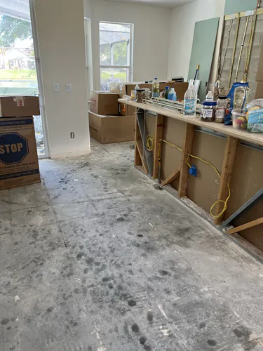Living room stripped to bare slab with a framed half wall carrying new wiring and packing boxes stacked against it