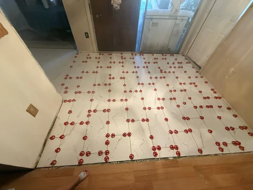 Large format marble look floor tile freshly set, with red leveling clips standing at every corner and joint