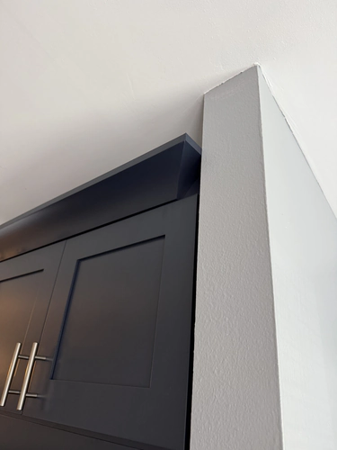 Close up of crown molding on a navy upper cabinet meeting a freshly painted grey wall return under a flat ceiling