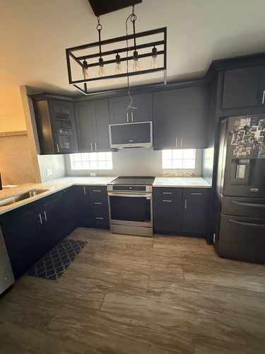 The same Orlando kitchen after the renovation, with navy shaker cabinets, a stainless range and microwave, and a black cage pendant light