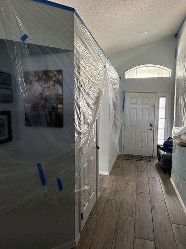 Hallway leading to the foyer and front door, with walls sheeted in plastic and the popcorn ceiling still in place