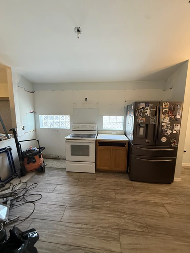 Kitchen with the cabinets and counters removed, patched drywall behind the range and two glass block windows
