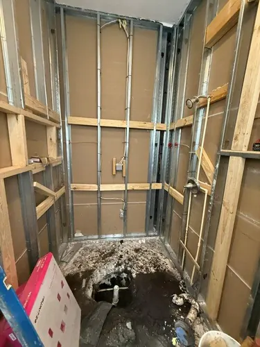 Shower stripped to steel studs and timber blocking with new supply lines roughed in and the drain open in the slab