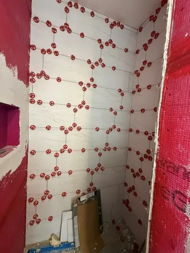 Marble look wall tile going up over the red waterproofing membrane, held flush by red leveling clips