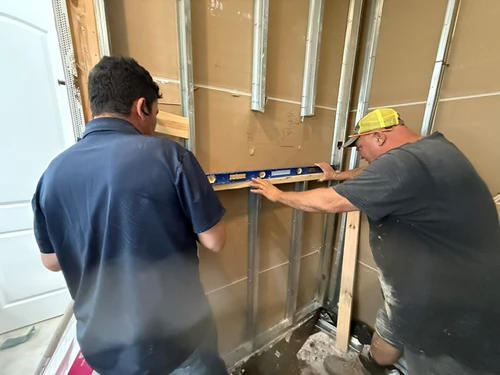 Two of the crew holding a spirit level against new shower framing to check it for plumb