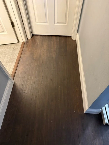 New plank flooring running into a hallway past white paneled doors, meeting the older tile at a transition strip