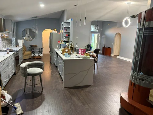 Open Orlando kitchen and living area after new plank flooring and repainting, with a stone island under a vaulted ceiling