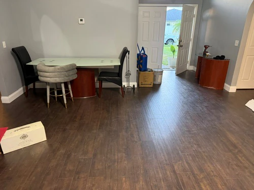 Finished living room with dark plank flooring, grey walls and white trim, looking towards the open front door