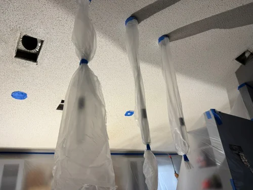Pendant lights bagged in plastic and taped off below a freshly textured ceiling